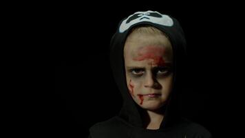 Halloween, en colère fille avec du sang maquillage sur affronter. enfant habillé comme effrayant squelette, poser, fabrication visages video
