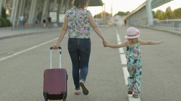 Mother and daughter walking outdoors to airport. Woman carrying suitcase bag. Child and mom vacation video