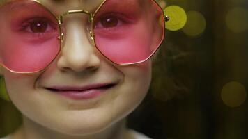 Close up face of child. Smiling, looking at camera. Girl in pink sunglasses posing video