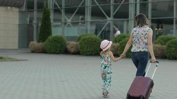 moeder en dochter wandelen naar luchthaven. vrouw draag- koffer tas. kind en mam vakantie. achterzijde video