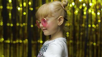 Child show thumbs up, smiling, looking at camera. Girl posing on background with foil golden curtain video