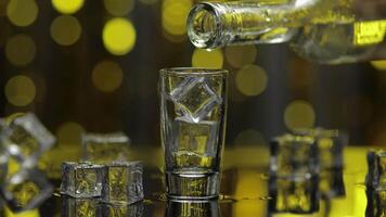 Barman pour frozen vodka from bottle into shot glass. Ice cubes against shiny gold party background video