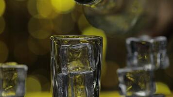 barman verser congelé Vodka de bouteille dans coup verre. la glace cubes contre brillant or fête Contexte video