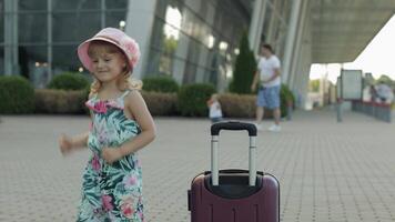 Child girl tourist with suitcase luggage bag near airport. Kid dances, rejoices, celebrates video