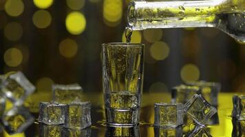 Barman pour frozen vodka from bottle into shot glass. Ice cubes against shiny gold party background video