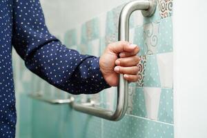 Asian woman patient use toilet support rail in bathroom, handrail safety grab bar, security in nursing hospital. photo