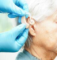 Doctor install hearing aid on senior patient ear to reduce hearing loss problem. photo