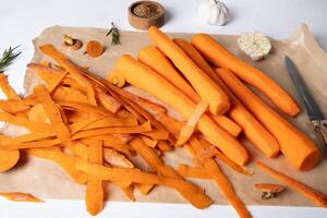 Peeled fresh raw carrots lie on parchment paper on the kitchen table. photo
