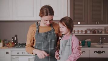 peu fille et maman sont en train de préparer gâteau dans le cuisine. ils sont dans une génial ambiance et ils sont en riant. video