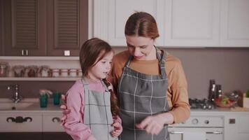 während Herstellung ein Kuchen, Mama Abstriche ihr Tochter Nase mit Creme, nach welche Sie lachen. ein jung Frau und ein Kind haben ein gut Zeit im das Küche im ihr Haus. glücklich Familie. video