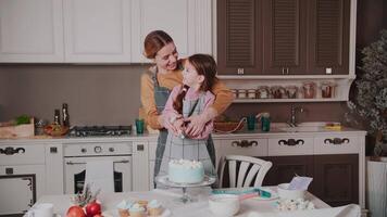 poco ragazza e mamma siamo preparazione torta nel il cucina. un' giovane donna e sua figlia spremere crema su un' torta. tenero sentimenti. ridere. vero emozioni. contento famiglia. video