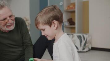 de kleinzoon Toneelstukken met zijn opa in speelgoed. bouwt een aannemer. de jongen is spelen Bij huis. schattig emoties in de kader. de verhaal van een familie. video