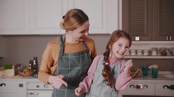 pequeño niña y mamá son preparando pastel en el cocina. ellos son en un genial estado animico y ellos son reír. video