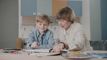 grootmoeder en kleinzoon zijn aan het doen huiswerk. portret van een gelukkig familie. aan het leren Bij huis. onderwijs. grootmoeder en kleinzoon lachen. schattig emoties in de kader. de verhaal van een familie. video