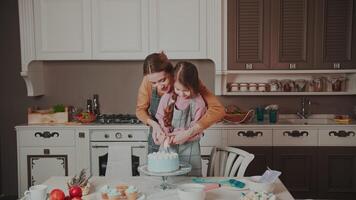 While making a cake, Mom laughingly smears her daughter's nose with cream. A young woman and a child have a good time in the kitchen in their house. Happy family. video