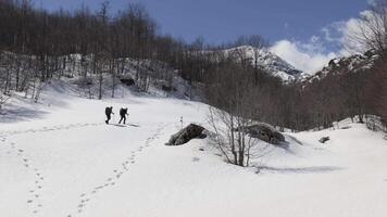 Two mountaineers hiking on a winter sunny day with some clouds on the horizon to reach the mountain peak. Walking on deep snow. video