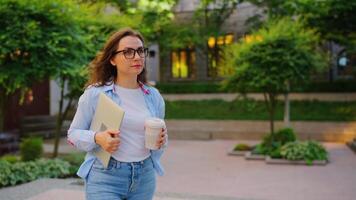Woman walking on street with laptop and coffee in hands after work day video