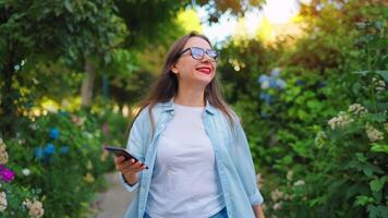 mujer con teléfono inteligente yendo en el floreciente jardín. video