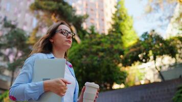 donna a piedi lungo il strada con il computer portatile e caffè nel mani dopo opera giorno video