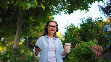 Woman with coffee and smartphone walking through the blooming garden video