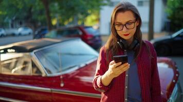 Woman is standing outdoors near the red vintage car and using smartphone video