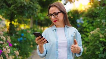 Woman with laptop and smartphone standing in the blooming garden video