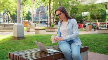 retrato do mulher sentado dentro a parque com computador portátil e café video