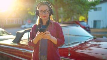 kvinna är stående utomhus nära de röd årgång bil och använder sig av smartphone video
