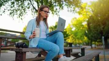Woman sitting in the park with laptop and coffee. Slow motion video