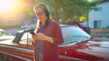 femme est permanent en plein air près le rouge ancien voiture et en utilisant téléphone intelligent video