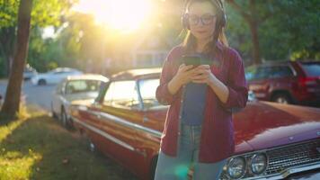 Woman is standing outdoors near the red vintage car and using smartphone video
