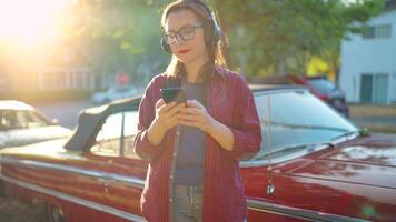 mujer es en pie al aire libre cerca el rojo Clásico coche y utilizando teléfono inteligente video