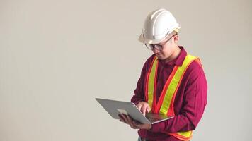 retrato de joven asiático ingeniero hombre trabajador con la seguridad uniforme blanco casco en pie participación ordenador portátil computadora cuaderno. datos tecnología dispositivo aislado en blanco antecedentes. video