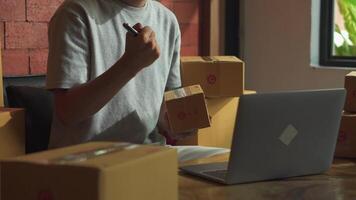 asiático hombre trabajando ordenador portátil computadora desde hogar piso con postal parcela, de venta en línea ideas concepto. video