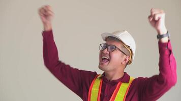 Handsome young asian engineer wearing orange vest and helmet over isolated white background.Celebrating surprised and amazed for success with arms raised. Winner concept. video