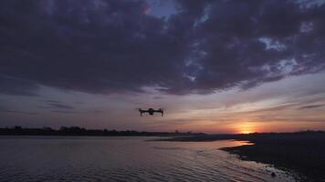 silhouette de moderne drone avec caméra en volant au dessus le rivière avec Contexte à le coucher du soleil. video