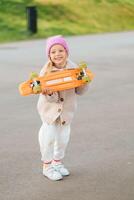 pequeño rubia niña paseos un patineta. elegante niña se ríe y patinetas foto