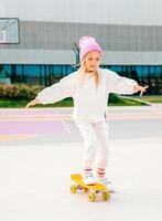 little blonde girl rides a skateboard. Stylish girl laughs and skateboards. photo