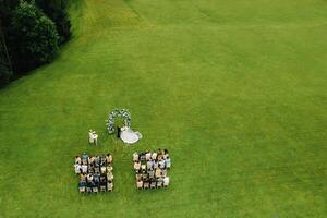 parte superior ver de el Boda ceremonia en un verde campo con invitados sentado en sillas. Boda lugar de eventos en el verde césped. foto