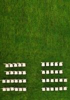 Top view of White wooden chairs standing in rows on a green field waiting for guests.View from a height of many white chairs standing on a green lawn photo