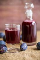 plum red wine in a glass and a decanter against the background of ripe large plums on the table. photo