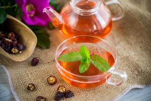 brewed rosehip tea in a glass teapot with rosehip flowers and mint photo