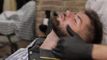 Client with black beard during beard shaving in barber shop. Groom, masculine video