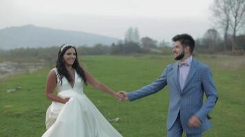 Wedding couple running near mountain river. Groom and bride in love video