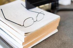 Glasses on pile book with computer on table photo