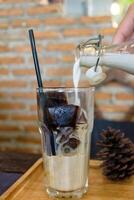 Ice coffee cubes with milk pouring into glass in cafe photo