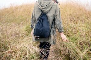 Rear young girl traveler with bag walking to golden meadow on mount photo