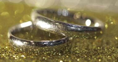 Wedding silver rings lying on shiny glossy surface. Shining with light. Close-up video