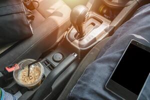 dentro coche con célula teléfono en conductor con café y cámara bolso para viaje foto