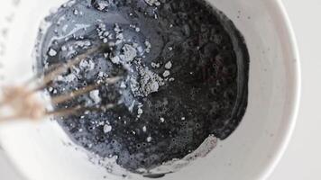 Mixing a Charcoal face mask with macro particles. A sample of a cosmetic scrub for cleansing the skin. Top view of black clay and mud face mask. Spa relaxation and enjoyment video